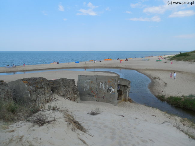 Uchodząca do morza niewielka rzeczka widziana z wydmy, przy niej szeroka plaża