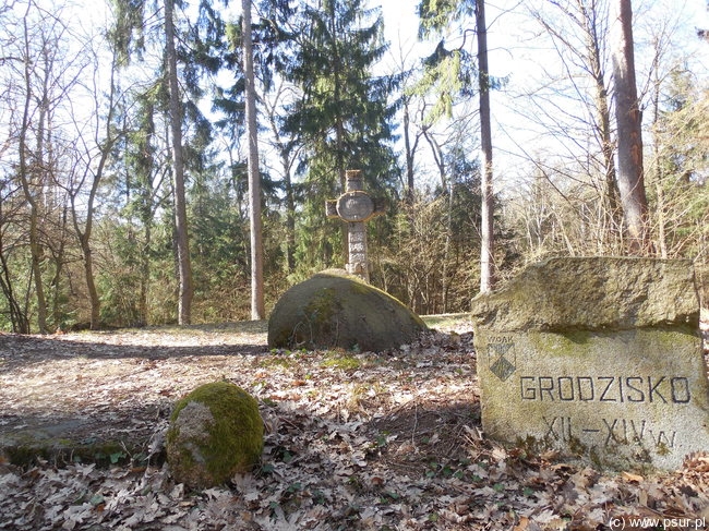 Kamienna tablica oznaczająca grodzisko, w tle krzyż