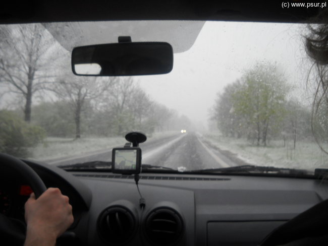 Widok zza szyby auta na zaśnieżoną drogę i pola