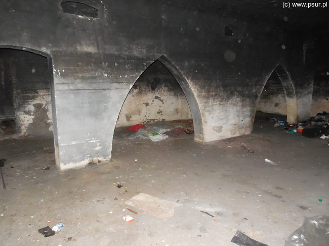 Ciemne wnętrze jednego z bunkrów: betonowe ściany, śmieci na podłodze