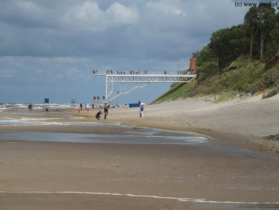 Plaża, w oddali biały taras widokowy, wychodzący wysoko z klifu