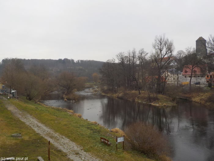 Rzeka, na jej brzegu na wzniesieniu domek i wieża zamku