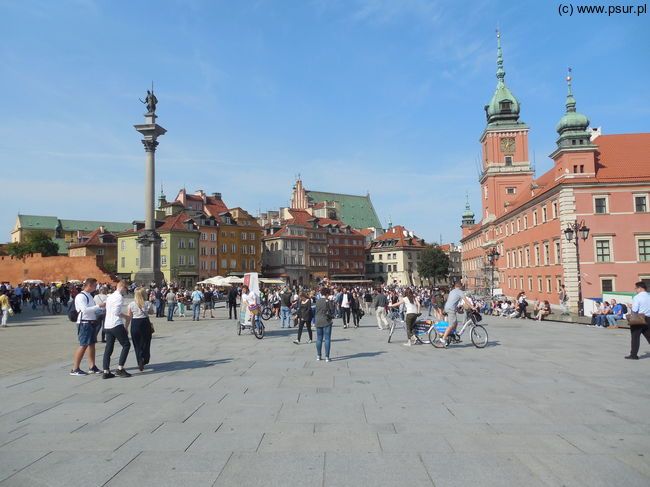 Zatłoczony plac zamkowy, po prawej fragment pomarańczowego Zamku Królewskiego, po lewej Kolumna Zygmunta